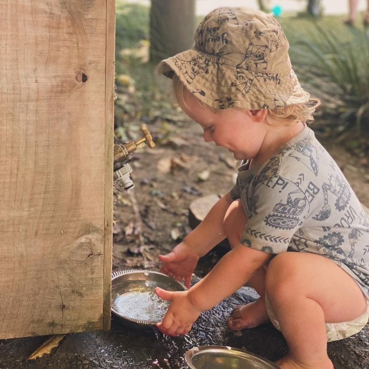 Young boy loving exploring with water outside at Busy Bees Hastings