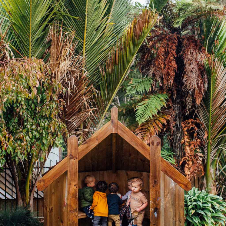 Outdoor playground with wooden hut for toddlers at Busy Bees Whau Valley 