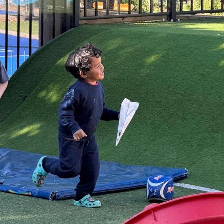 Little boy running around with paper airplane at Grey Lynn Montessori by Busy Bees